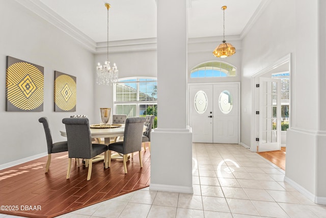 foyer entrance with an inviting chandelier, a towering ceiling, decorative columns, ornamental molding, and light hardwood / wood-style floors