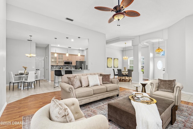 living room featuring decorative columns, ceiling fan with notable chandelier, and light hardwood / wood-style flooring