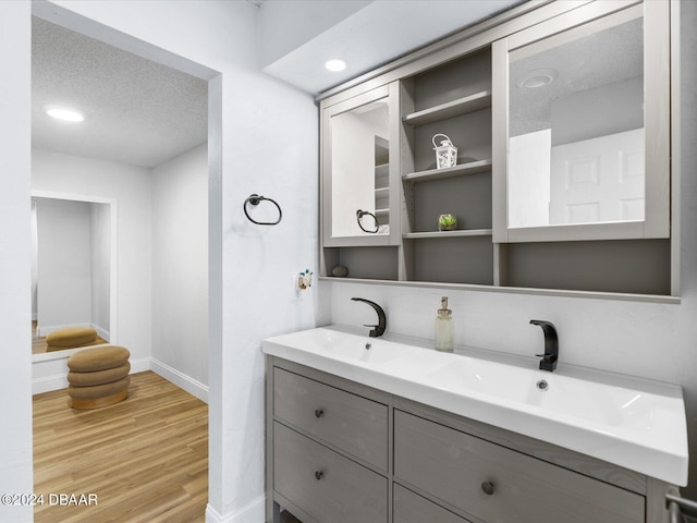 bathroom featuring a textured ceiling, a sink, wood finished floors, baseboards, and double vanity