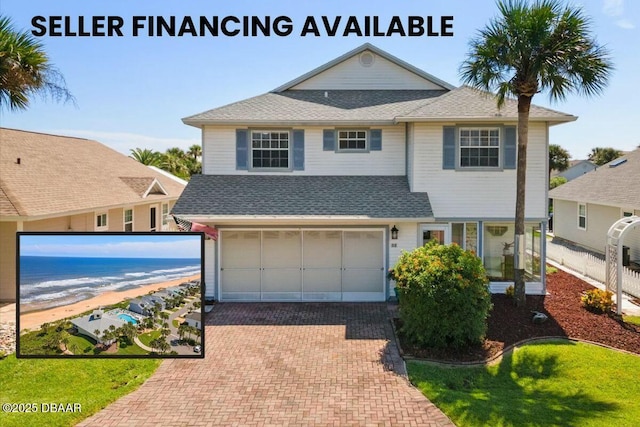 traditional home with decorative driveway, a shingled roof, a view of the beach, a water view, and a garage