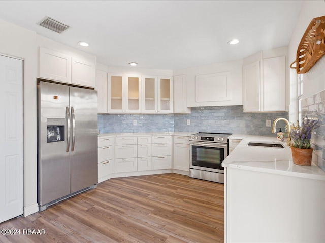 kitchen with appliances with stainless steel finishes, glass insert cabinets, a sink, and white cabinetry