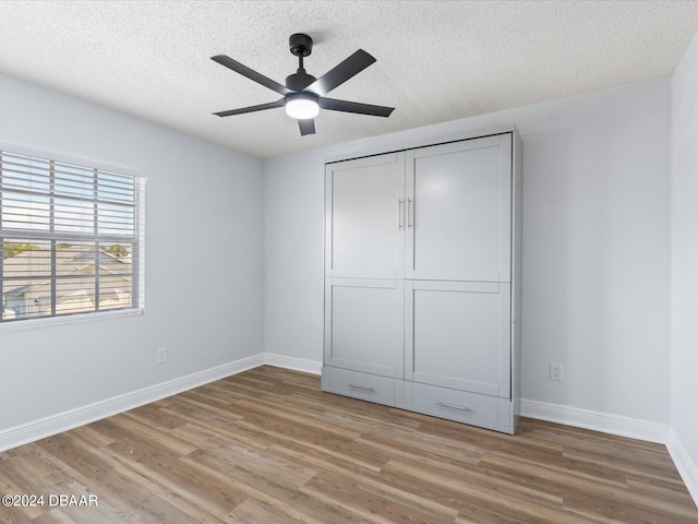 unfurnished bedroom with baseboards, ceiling fan, a textured ceiling, light wood-type flooring, and a closet