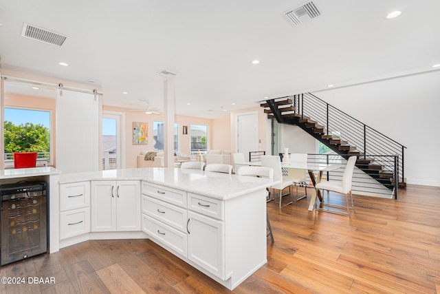 kitchen featuring wine cooler, a barn door, a healthy amount of sunlight, white cabinets, and light hardwood / wood-style flooring