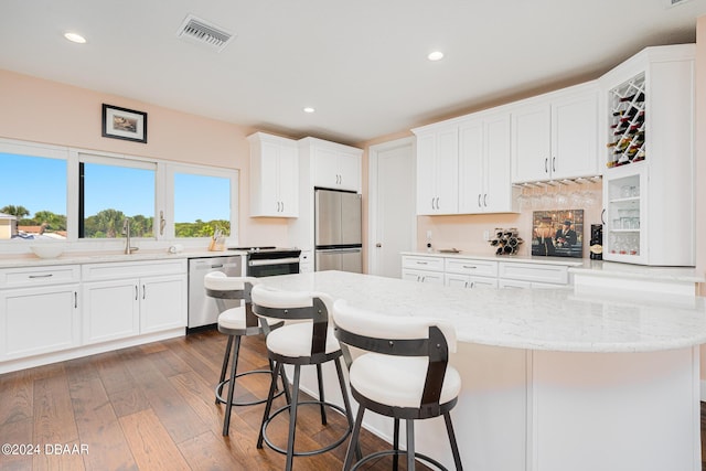 kitchen with light stone countertops, white cabinetry, appliances with stainless steel finishes, and a kitchen bar