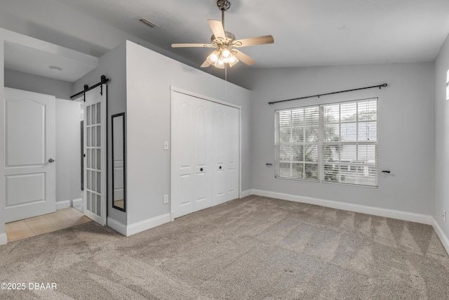 unfurnished bedroom with light carpet, a barn door, ceiling fan, a closet, and lofted ceiling