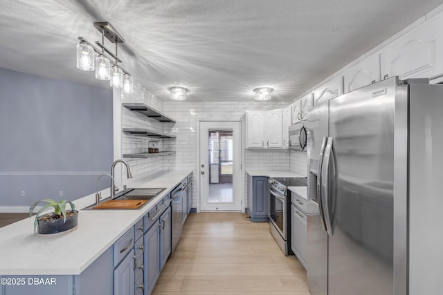 kitchen with white cabinets, appliances with stainless steel finishes, decorative backsplash, blue cabinetry, and sink