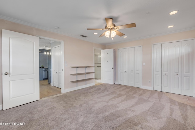 unfurnished bedroom featuring ceiling fan, light colored carpet, multiple closets, and ornamental molding