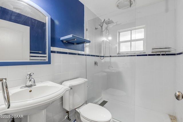 bathroom with sink, tile walls, toilet, and a tile shower