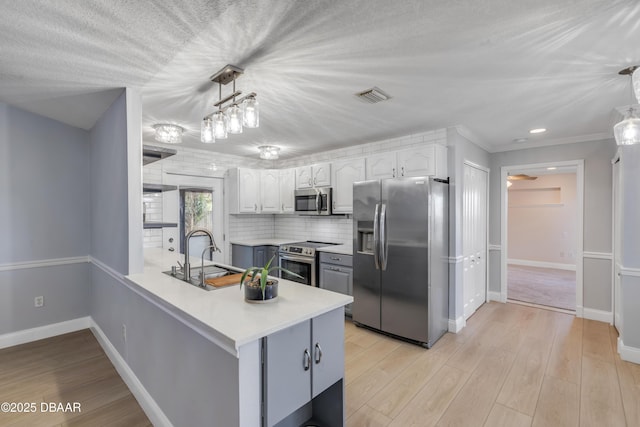 kitchen featuring kitchen peninsula, appliances with stainless steel finishes, decorative light fixtures, white cabinets, and sink