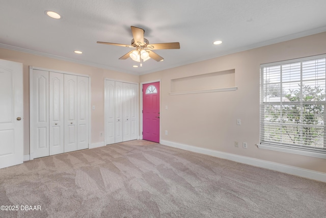 unfurnished bedroom with ceiling fan, light carpet, crown molding, and two closets