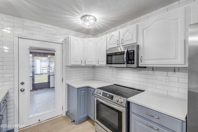 kitchen with a textured ceiling, appliances with stainless steel finishes, backsplash, and white cabinets