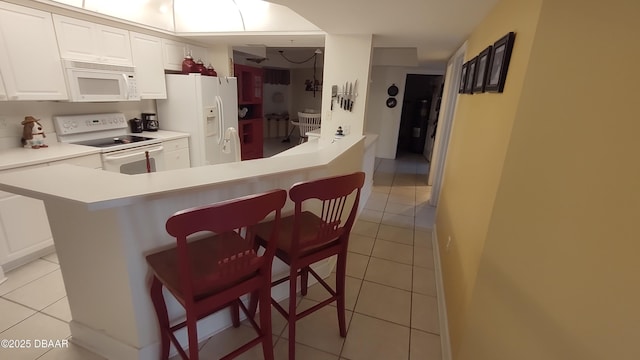 kitchen with white appliances, white cabinets, light countertops, a kitchen bar, and light tile patterned flooring