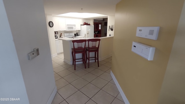 kitchen with a breakfast bar, white cabinets, light tile patterned flooring, white appliances, and baseboards