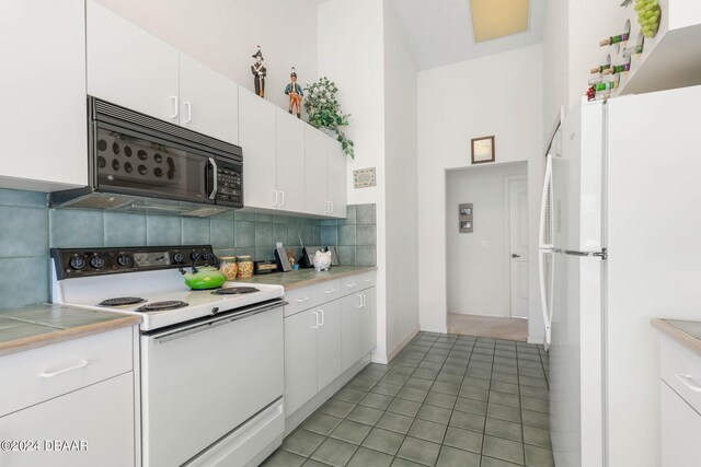 kitchen featuring white cabinetry, decorative backsplash, light tile patterned flooring, and white appliances