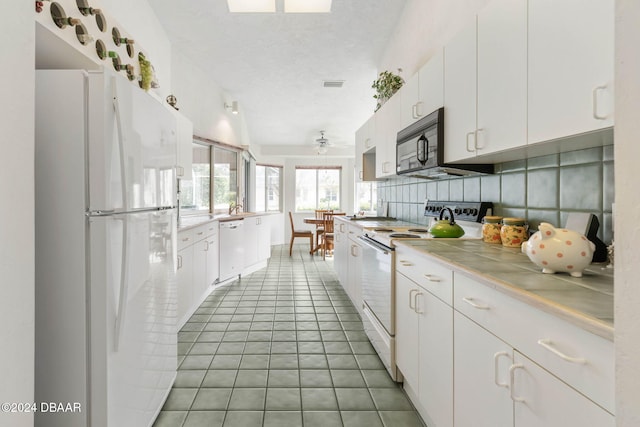 74 Kingsley Ln, Ormond Beach, FL 32174 - kitchen with white appliances, white cabinets, light tile patterned flooring, tasteful backsplash, and tile countertops