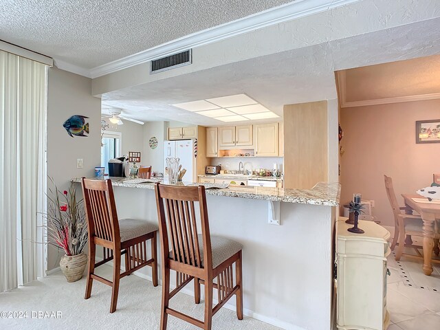 kitchen featuring light stone counters, light carpet, white refrigerator, and a kitchen bar