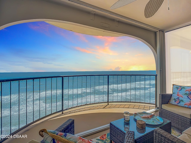 balcony at dusk with outdoor lounge area, a water view, and ceiling fan