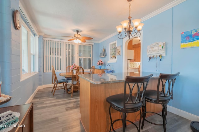 kitchen with stone countertops, ornamental molding, ceiling fan with notable chandelier, decorative light fixtures, and hardwood / wood-style floors