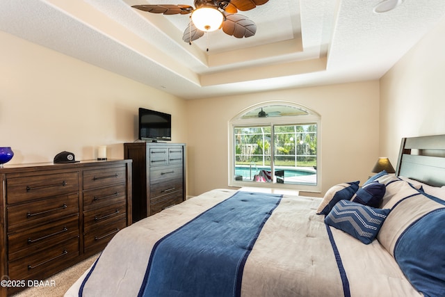 bedroom with access to outside, ceiling fan, a raised ceiling, light carpet, and a textured ceiling