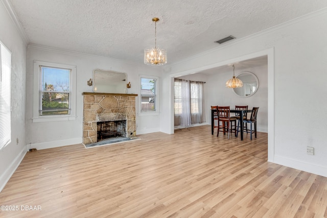 living room with hardwood / wood-style flooring, crown molding, an inviting chandelier, a textured ceiling, and a stone fireplace