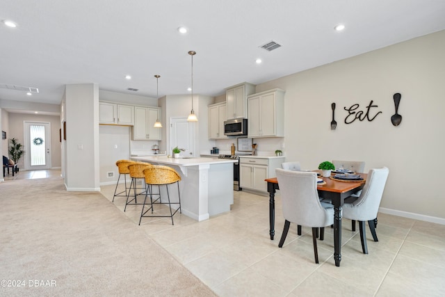 kitchen featuring light carpet, electric range oven, a breakfast bar, a kitchen island with sink, and decorative light fixtures