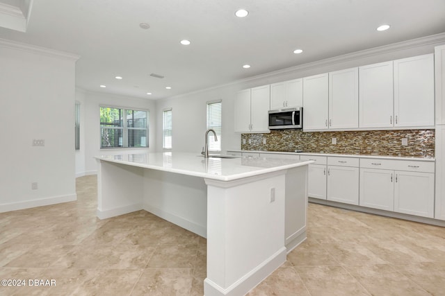 kitchen with backsplash, ornamental molding, sink, a center island with sink, and white cabinets