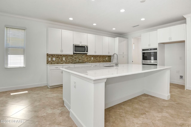 kitchen with white cabinets, stainless steel appliances, tasteful backsplash, and an island with sink