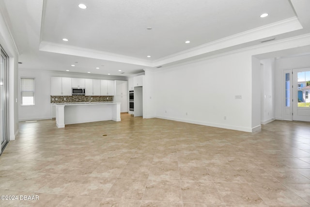 unfurnished living room with a tray ceiling, a wealth of natural light, and ornamental molding