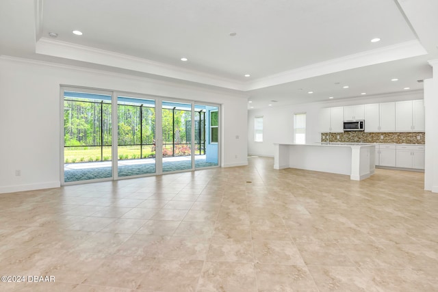 unfurnished living room featuring a raised ceiling, light tile patterned floors, and ornamental molding