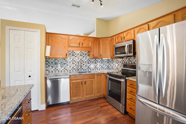 kitchen featuring appliances with stainless steel finishes, light stone counters, a textured ceiling, dark wood-type flooring, and sink