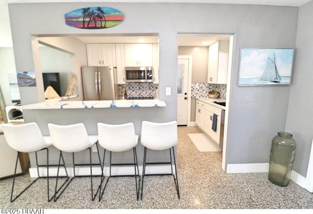 kitchen with a breakfast bar, kitchen peninsula, stainless steel appliances, decorative backsplash, and white cabinets