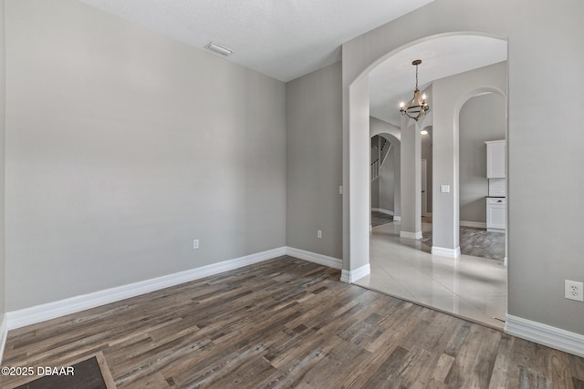 spare room with a chandelier and dark wood-type flooring