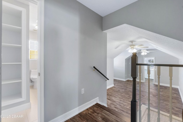 staircase with ceiling fan, lofted ceiling, wood-type flooring, and a textured ceiling