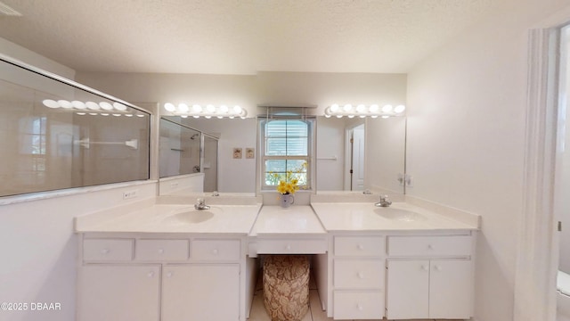 bathroom with double vanity, a shower stall, a textured ceiling, and a sink