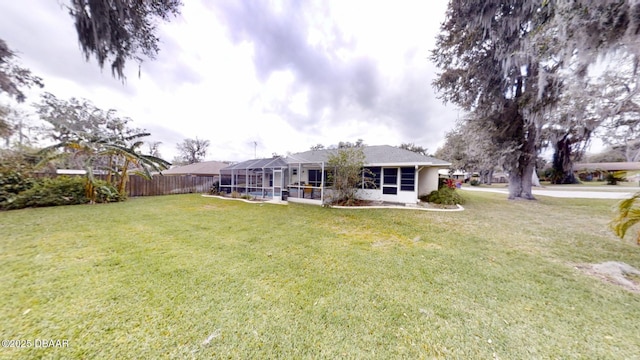 rear view of house featuring a lanai, fence, and a yard