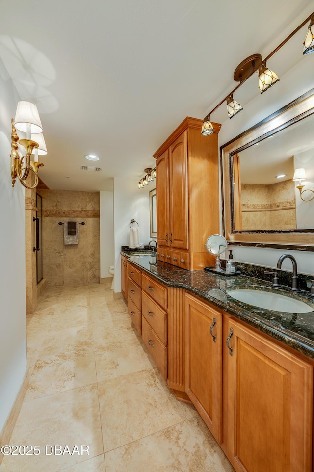 bathroom with vanity, tiled shower, and toilet