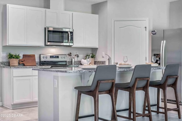 kitchen featuring white cabinetry, appliances with stainless steel finishes, a breakfast bar area, and dark stone counters