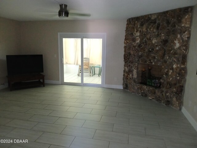 unfurnished living room featuring a stone fireplace, ceiling fan, and light tile patterned floors