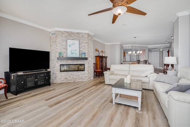 living room with crown molding, a stone fireplace, ceiling fan with notable chandelier, and light wood-type flooring