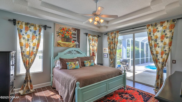 bedroom with wood finished floors, baseboards, access to exterior, a textured ceiling, and a raised ceiling