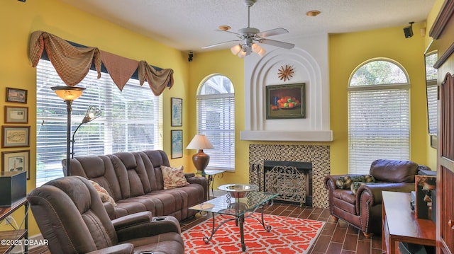 living area with dark wood-style floors, a tile fireplace, a textured ceiling, and ceiling fan