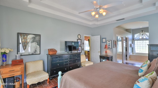 bedroom with arched walkways, visible vents, connected bathroom, and a tray ceiling