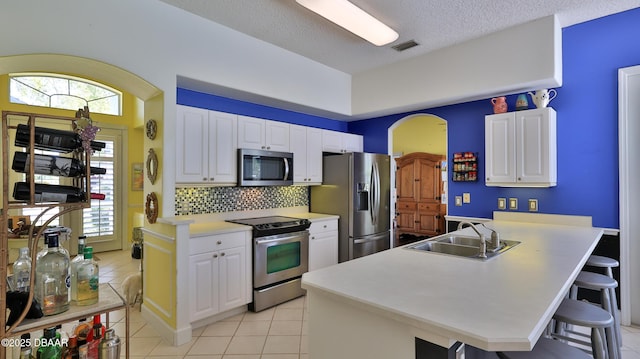 kitchen with visible vents, a peninsula, a sink, appliances with stainless steel finishes, and a kitchen bar