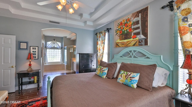 bedroom featuring visible vents, wood finished floors, arched walkways, a raised ceiling, and ceiling fan