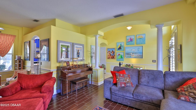 living area featuring decorative columns, wood finished floors, visible vents, and wainscoting