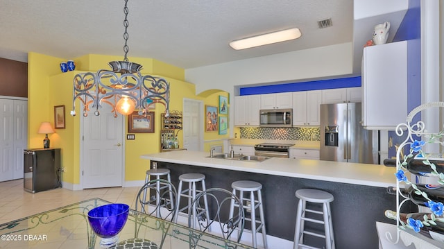 kitchen with visible vents, a sink, white cabinetry, stainless steel appliances, and a breakfast bar area