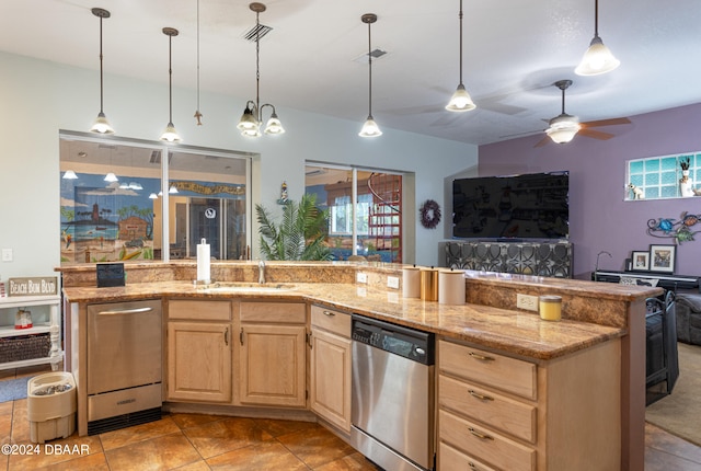 kitchen featuring sink, light stone counters, light brown cabinetry, stainless steel dishwasher, and hanging light fixtures