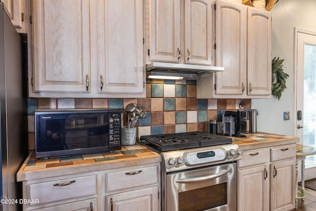 kitchen featuring butcher block counters, light brown cabinetry, appliances with stainless steel finishes, and decorative backsplash