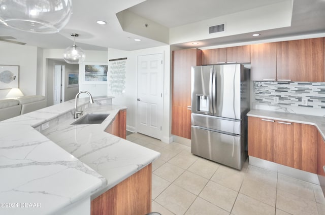 kitchen with hanging light fixtures, sink, tasteful backsplash, stainless steel fridge with ice dispenser, and light stone countertops