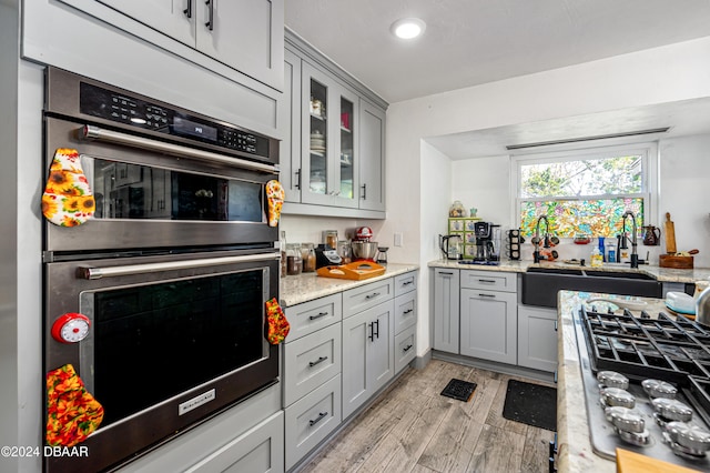 kitchen featuring sink, stainless steel double oven, light stone counters, gray cabinets, and light wood-type flooring